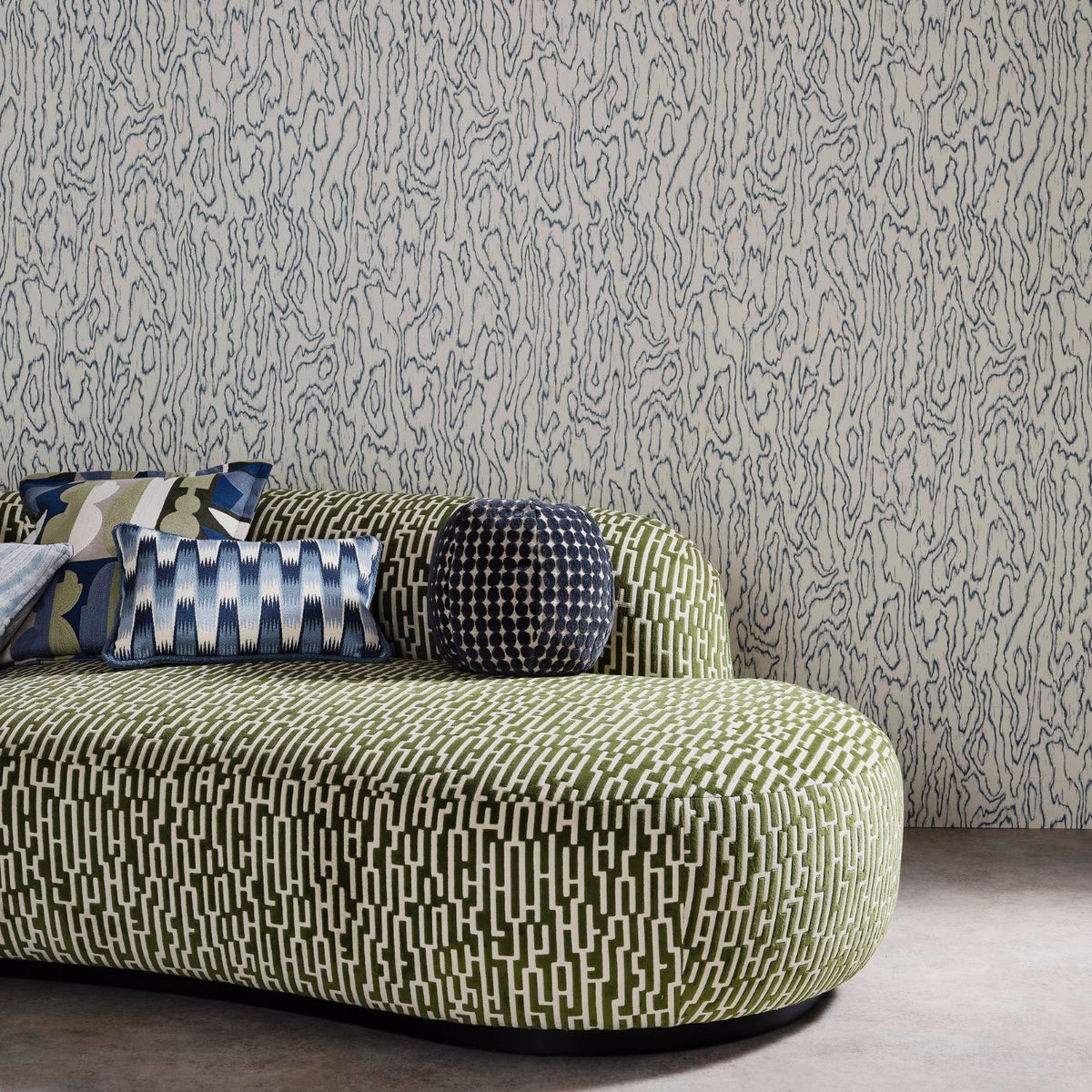 Edenfield wallpaper by Harlequin in a grey wood-grain moire design, styled behind a green sculptural sofa in a living room