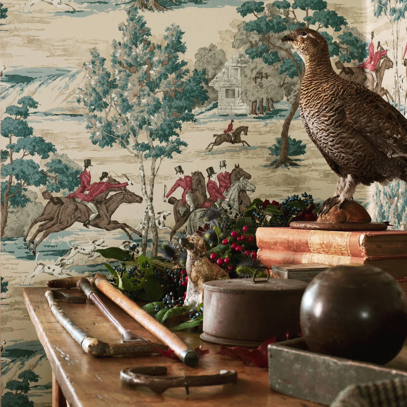 Tally Ho Teal wallpaper by Sanderson styled in a study with a taxidermy game bird, antique books and foliage on a timber table