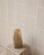 Woven Grid wallpaper in grey behind a sculptural vase on a plinth
