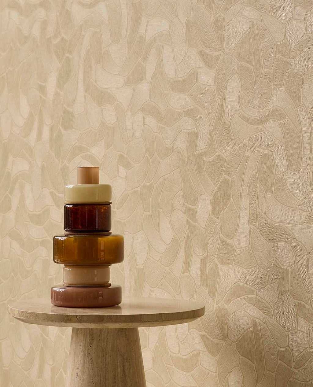Pebble Relief wallpaper in beige behind amber glassware on a stone side table