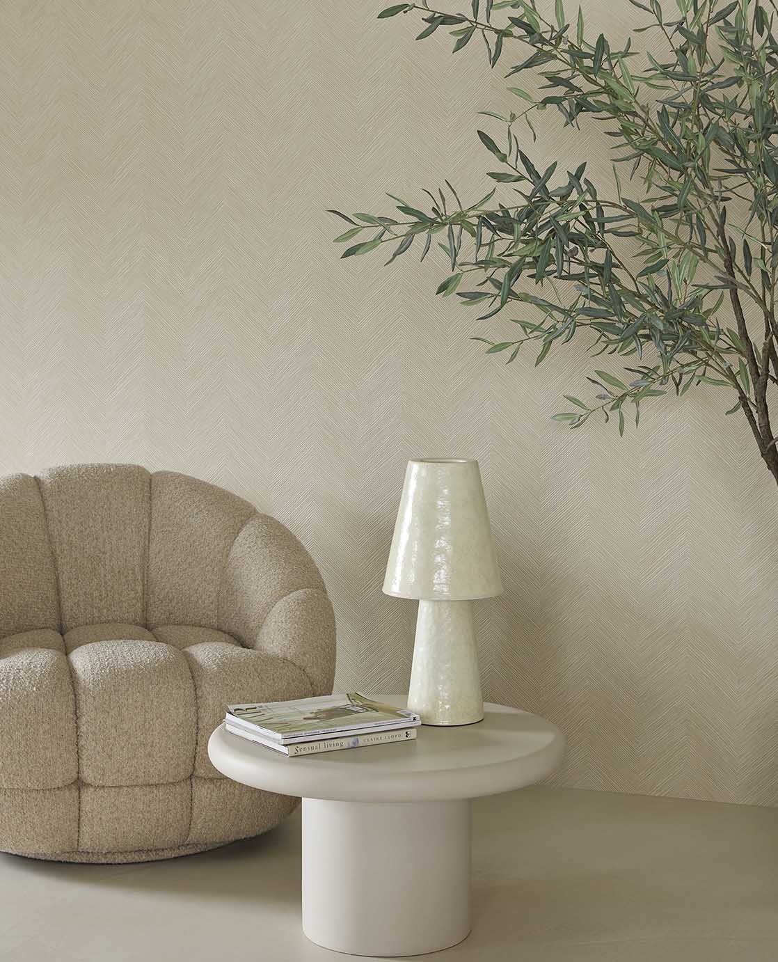 Woven Herringbone wallpaper in beige behind a boucle armchair and side table lamp