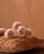 Raked Sand wallpaper in terracotta orange behind a cushion and flowers