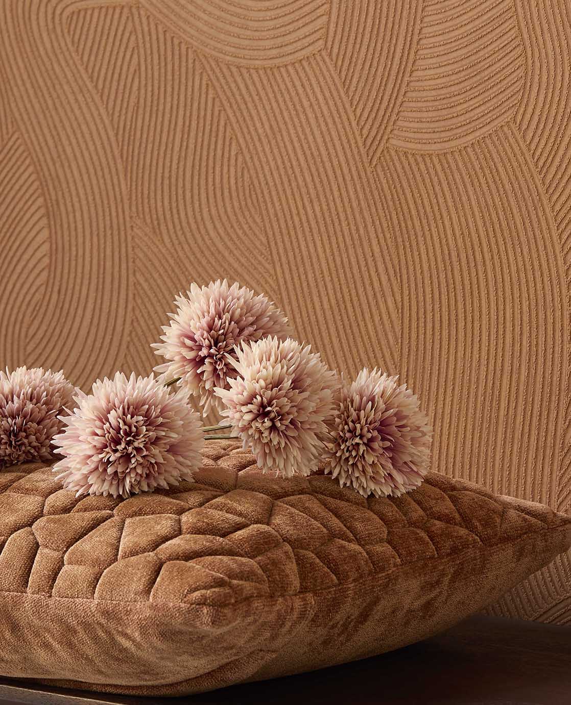 Raked Sand wallpaper in terracotta orange behind a cushion and flowers