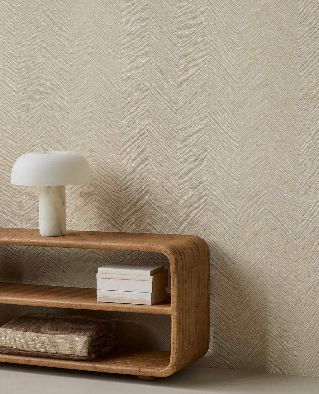 Woven Herringbone wallpaper in pale linen beige behind a curved timber console and lamp