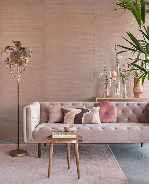 Paper Weave wallpaper by Eijffinger in blush pink, styled in a living room behind a tufted velvet sofa with a gold palm floor lamp.