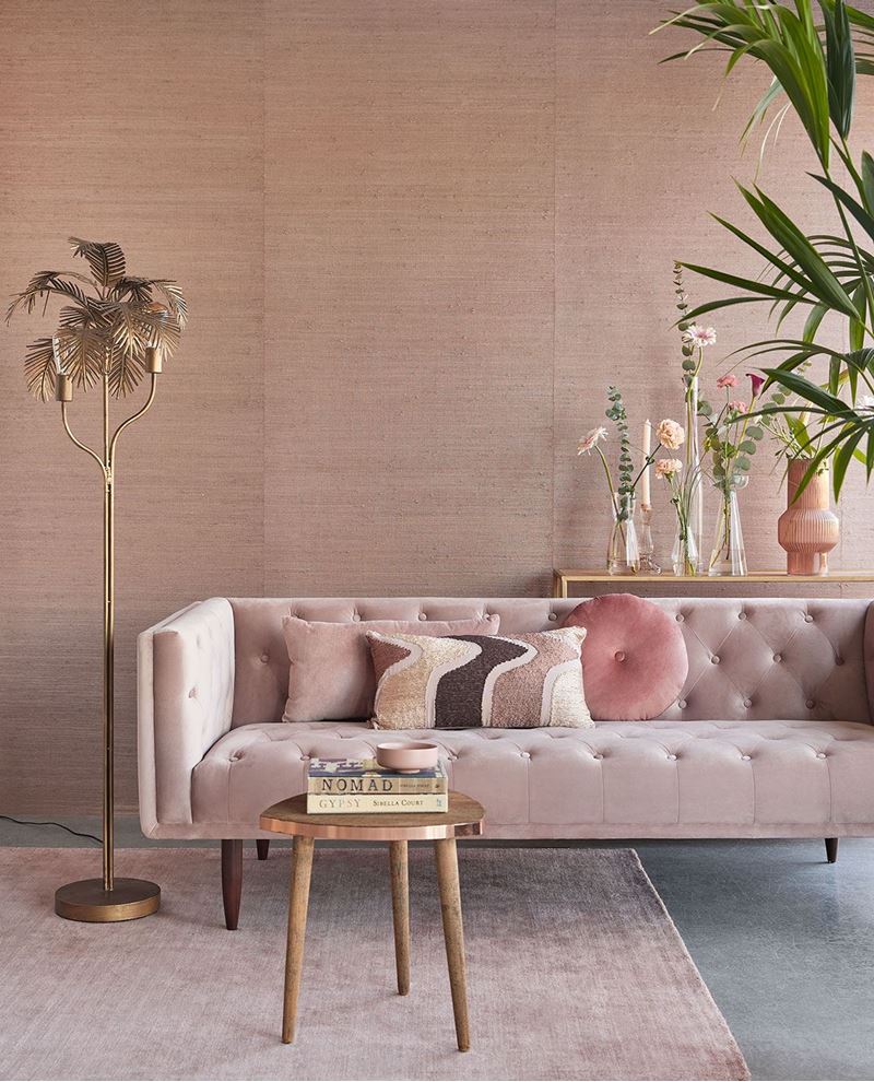 Paper Weave wallpaper by Eijffinger in blush pink, styled in a living room behind a tufted velvet sofa with a gold palm floor lamp.