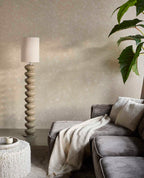 Pebble Relief wallpaper in beige behind a grey sofa, floor lamp and plant in a living room