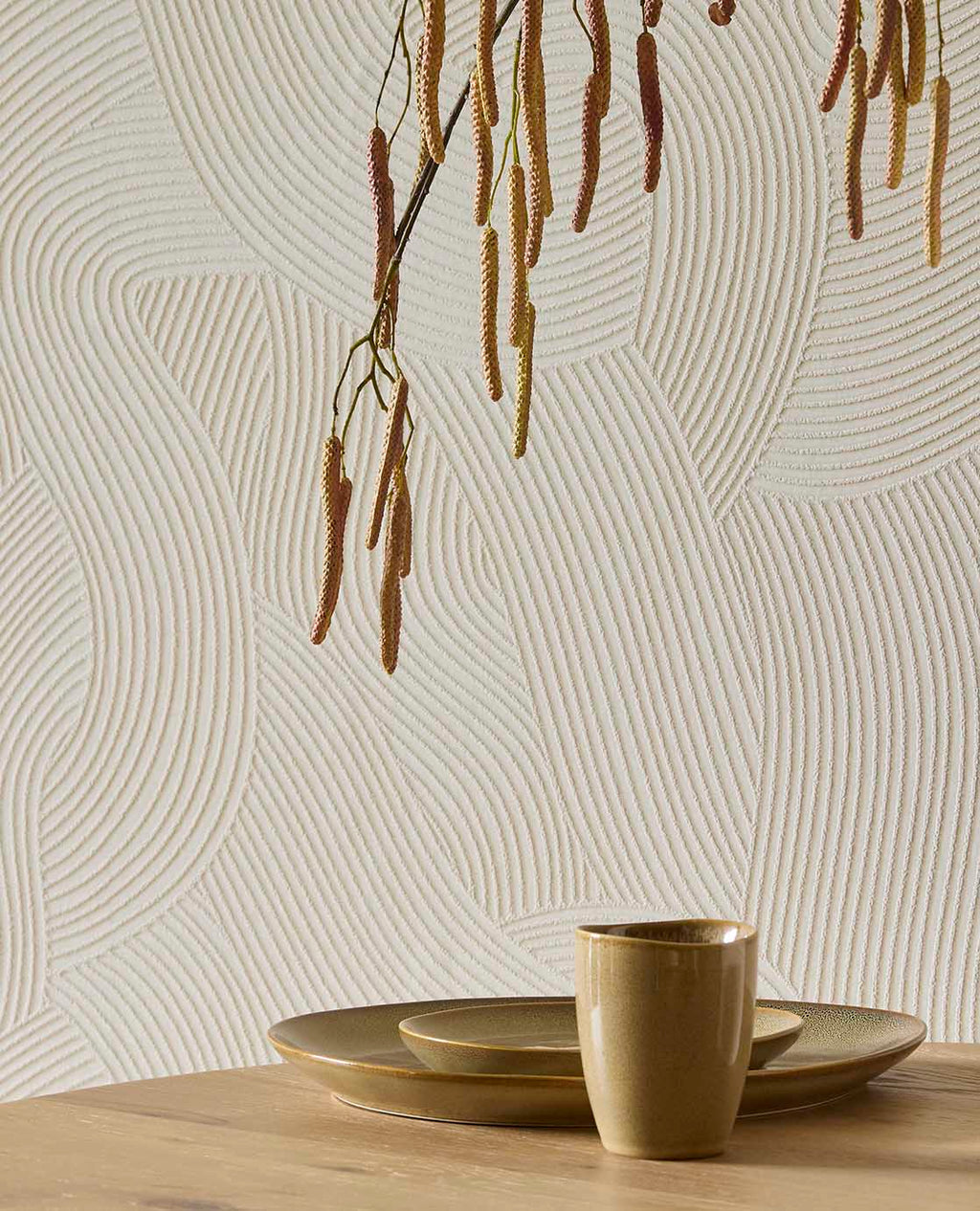Raked Sand wallpaper in cream behind a timber table with ceramics and hanging branches