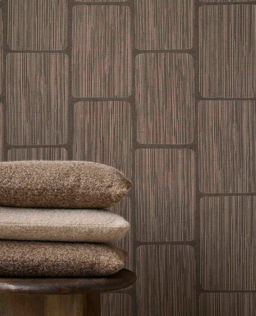 Woven Grid wallpaper in dark brown behind stacked cushions, close-up