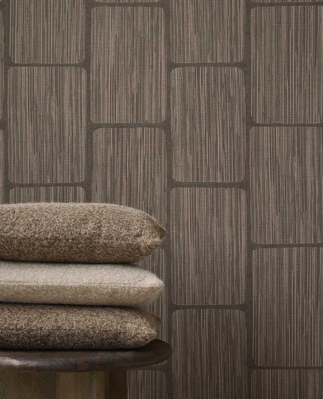 Woven Grid wallpaper in dark brown behind stacked cushions, close-up