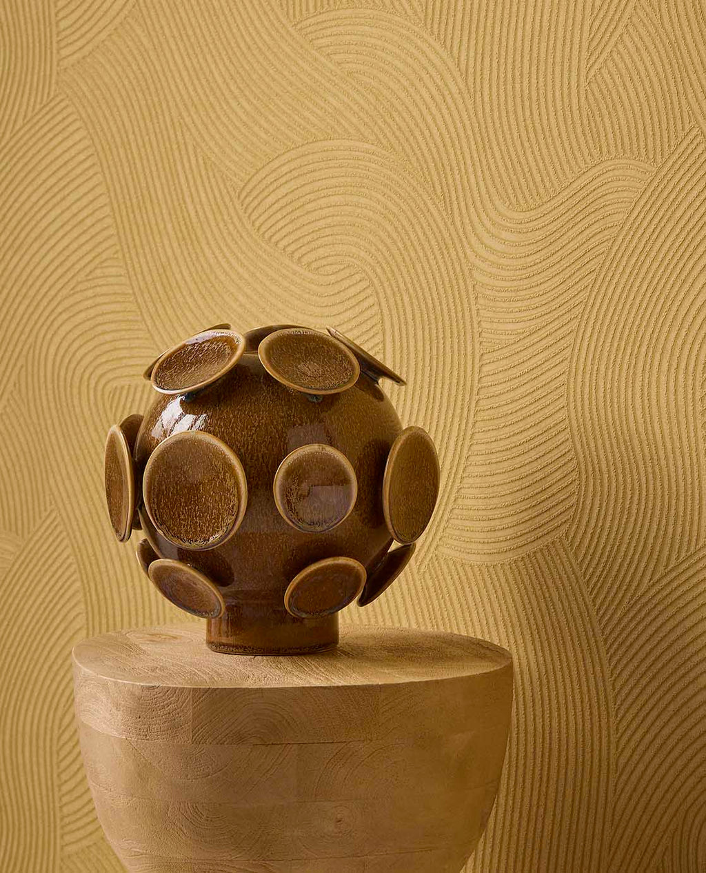 Raked Sand wallpaper in mustard yellow behind a ceramic sculpture on a timber plinth