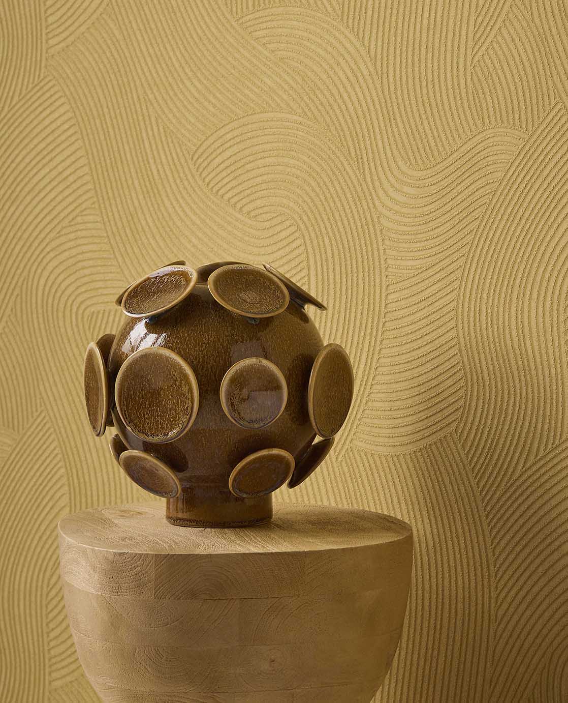 Raked Sand wallpaper in mustard yellow behind a ceramic sculpture on a timber plinth