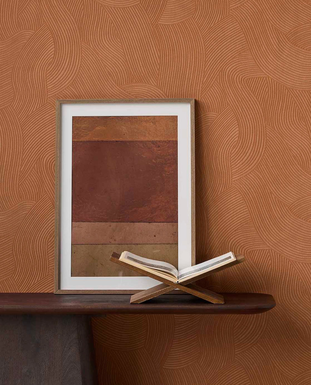 Raked Sand wallpaper in terracotta orange behind framed art on a dark console