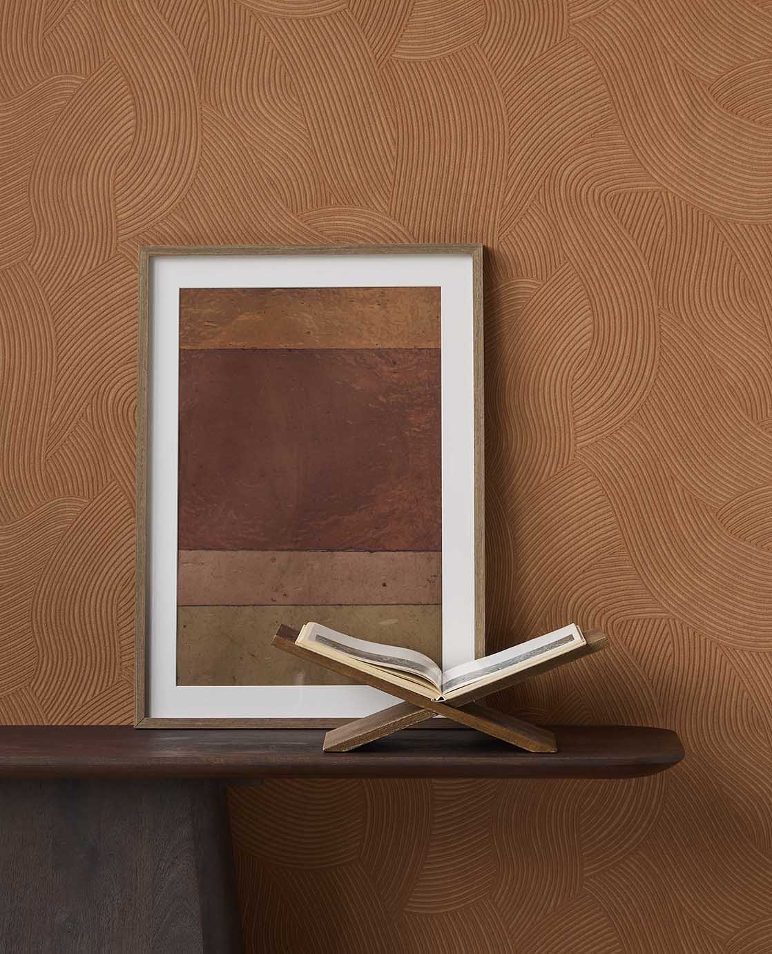 Raked Sand wallpaper in terracotta orange behind framed art on a dark console