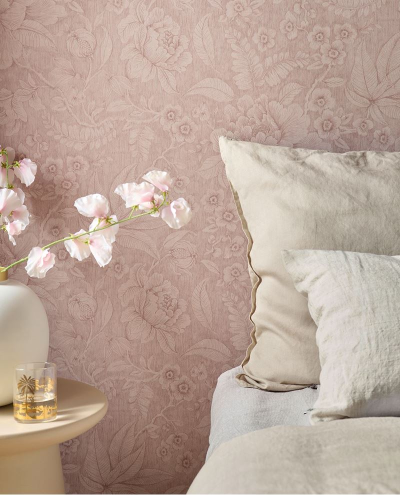 Tonal Rose wallpaper by Eijffinger styled behind a bed, soft dusty-pink floral pattern with linen pillows and a bedside vase of blossoms.