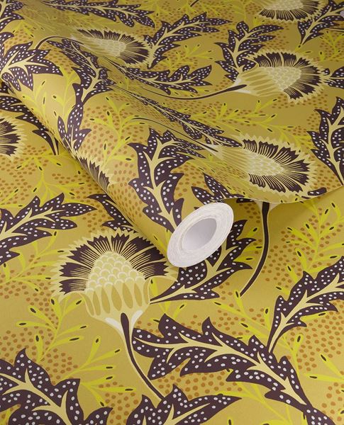 Banksia Bloom wallpaper by Eijffinger in mustard yellow with aubergine thistle blooms, shown on a curled swatch