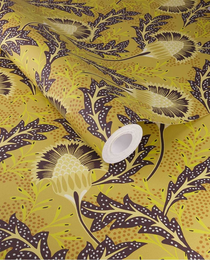Banksia Bloom wallpaper by Eijffinger in mustard yellow with aubergine thistle blooms, shown on a curled swatch