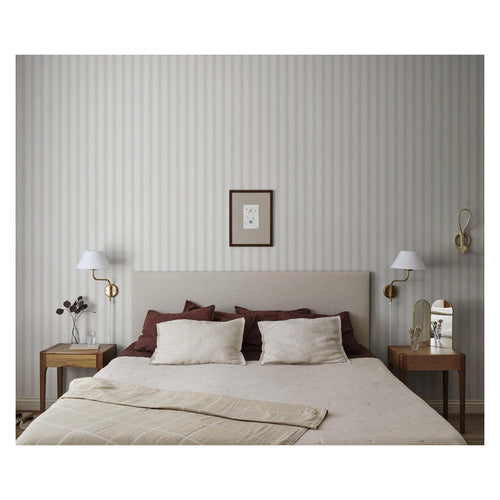 Gustav Stripe wallpaper by Sandberg in soft dove grey, behind an upholstered bed with brass wall lamps in a calm bedroom