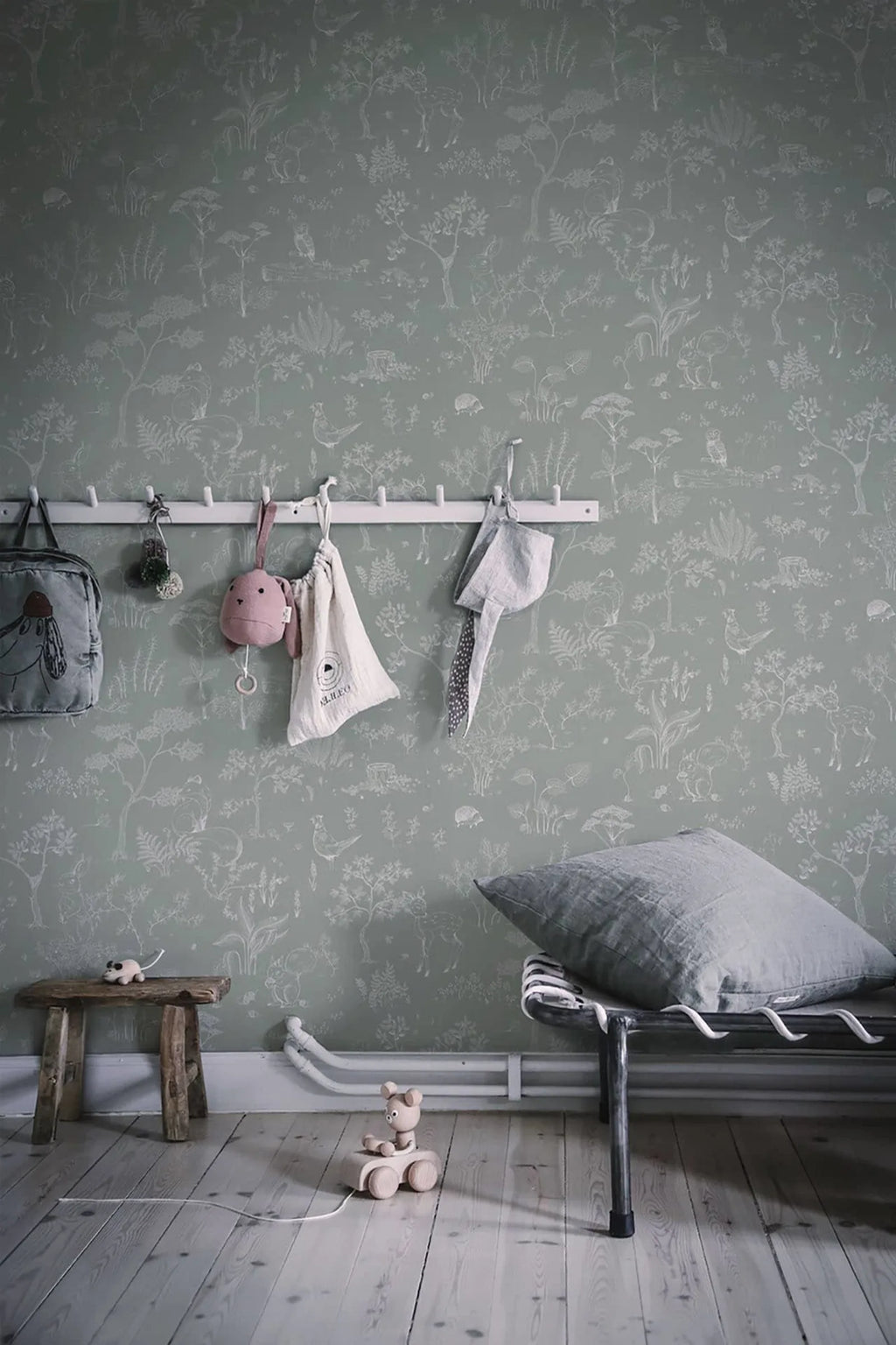 Hollie wallpaper by Sandberg in sage green woodland print behind a peg rail and metal daybed in a kids room