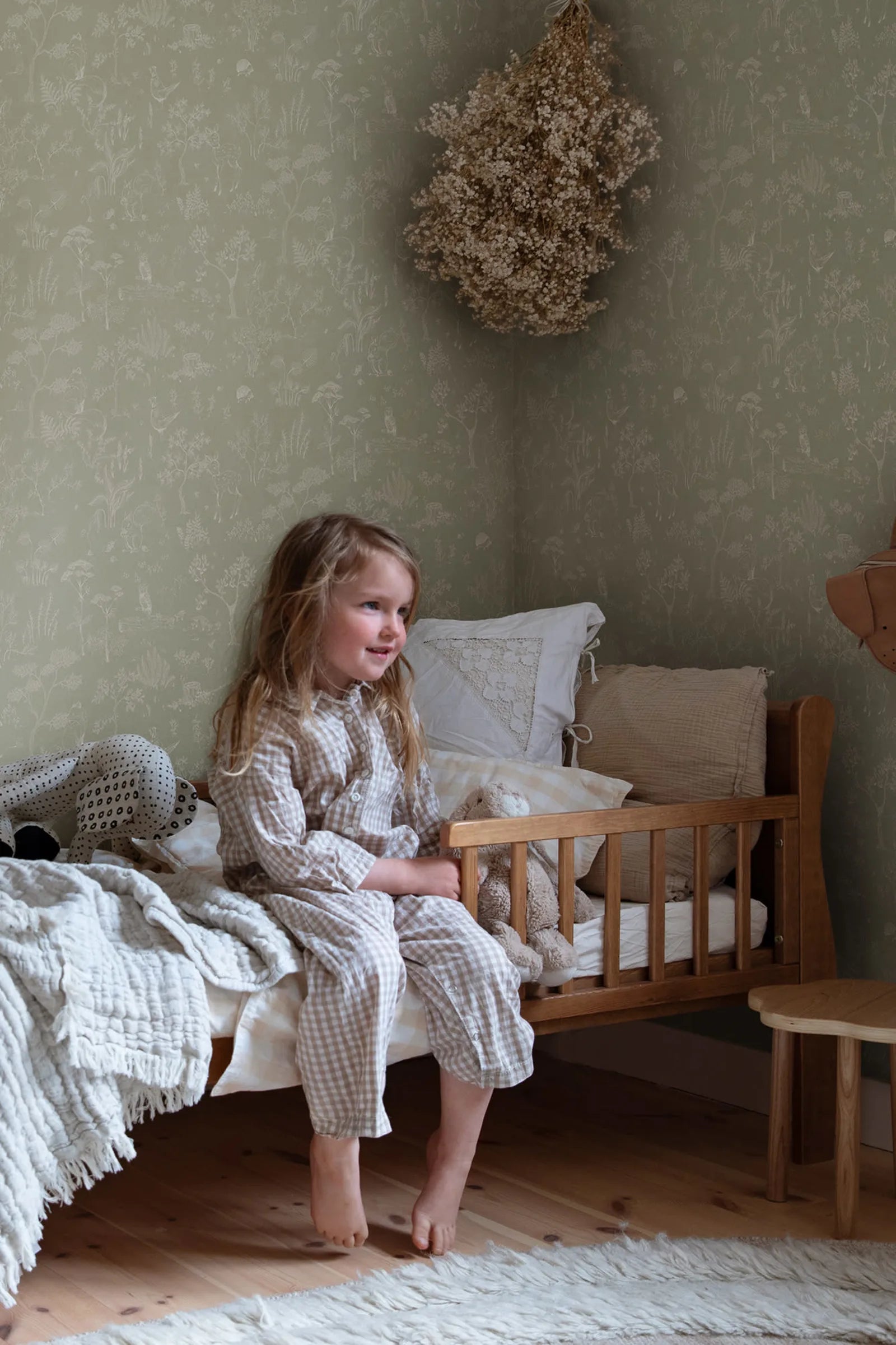 Hollie wallpaper by Sandberg in sage green woodland print in a cosy child bedroom corner with wooden cot bed