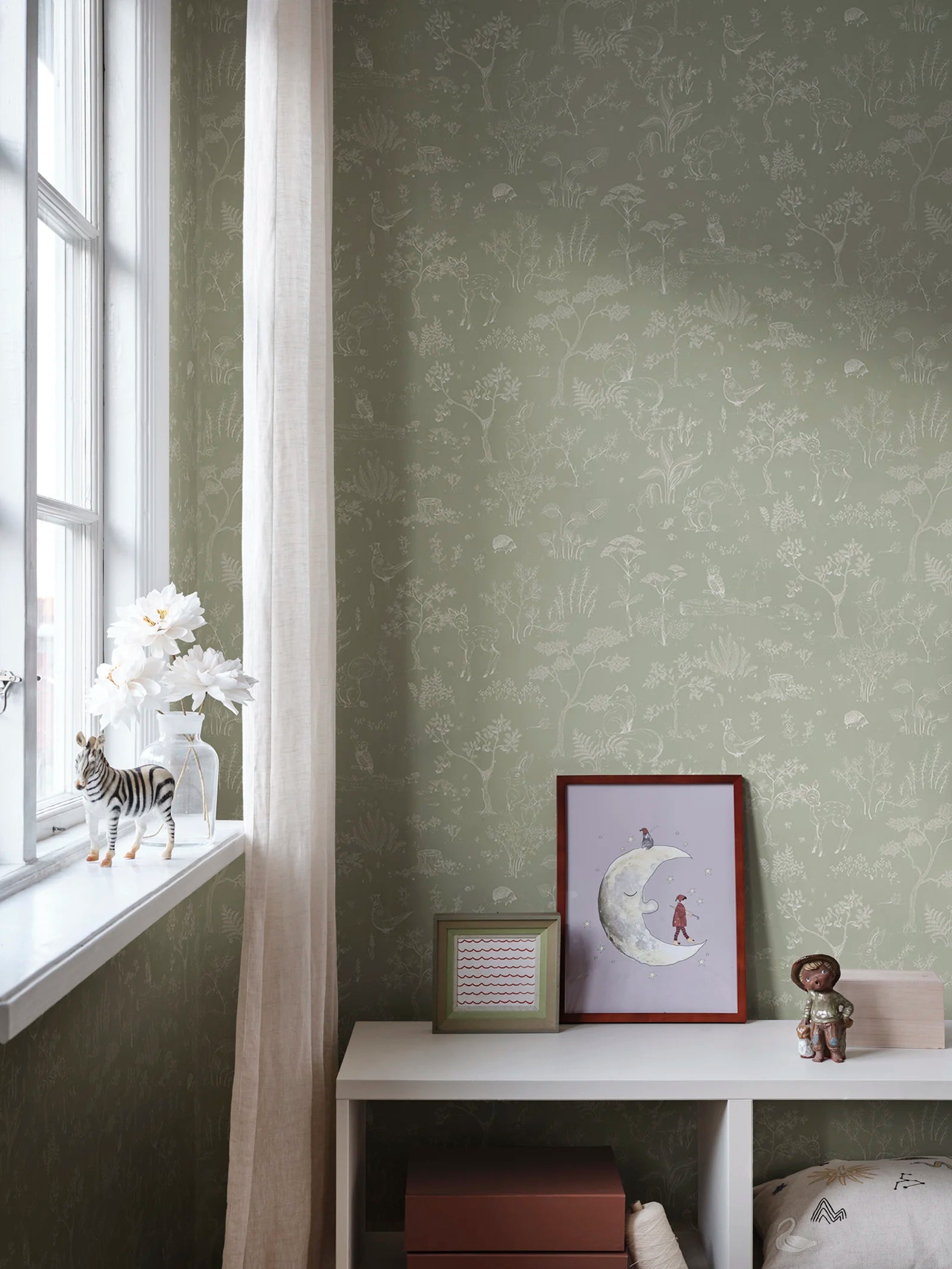 Hollie wallpaper by Sandberg in sage green woodland print by a bright window with childrens art and toy zebra