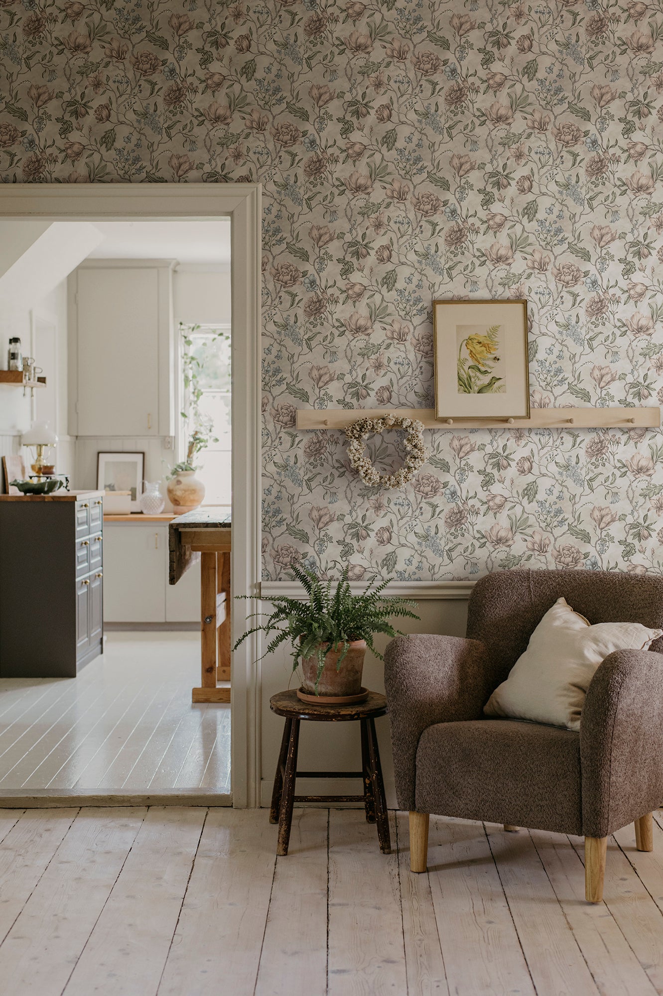 Linda wallpaper by Sandberg in soft greige in a living room with a boucle armchair, framed botanical print and wreath