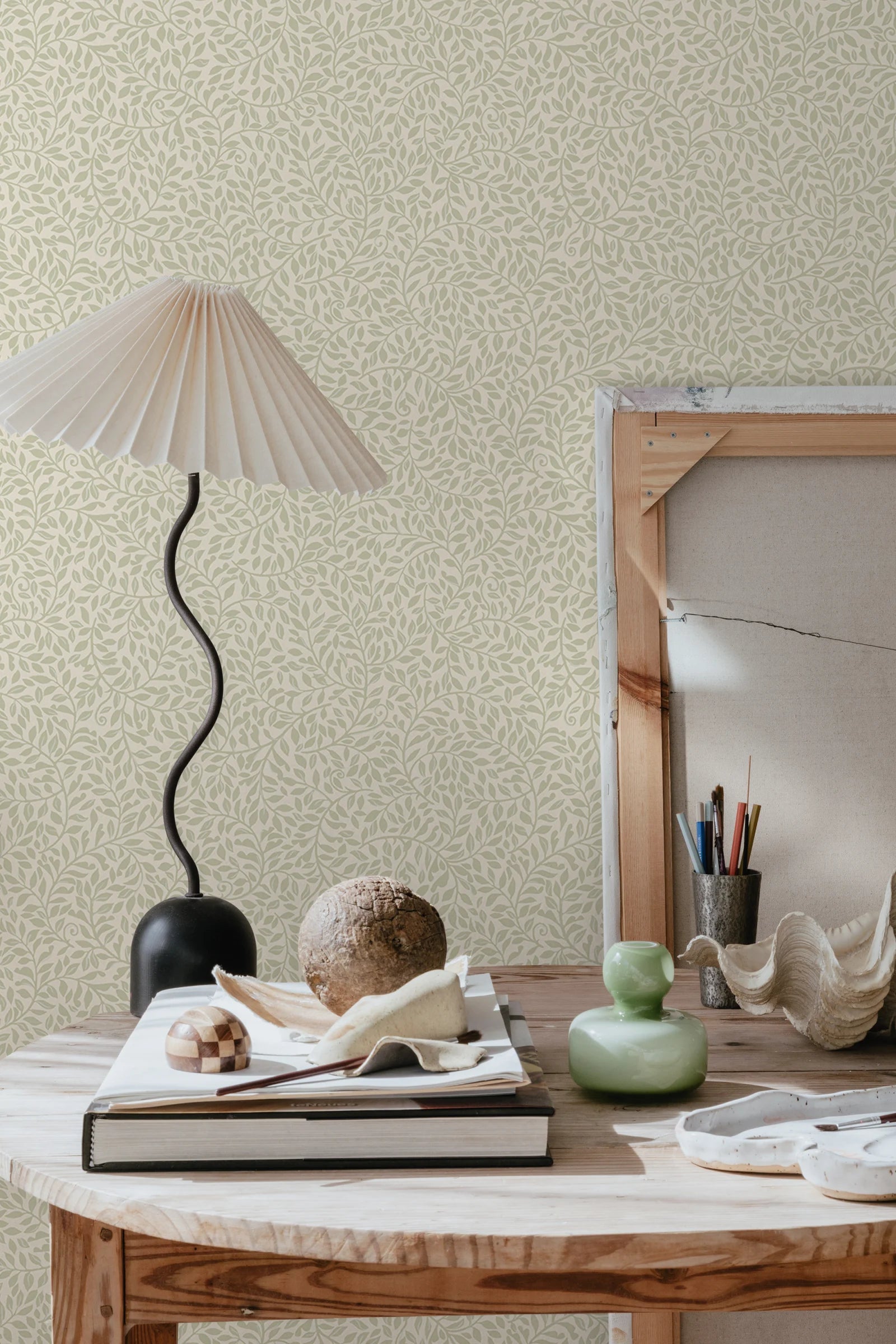 Sigfrid wallpaper by Sandberg in sage on cream, styled behind a wooden desk with a wavy black lamp and ceramics