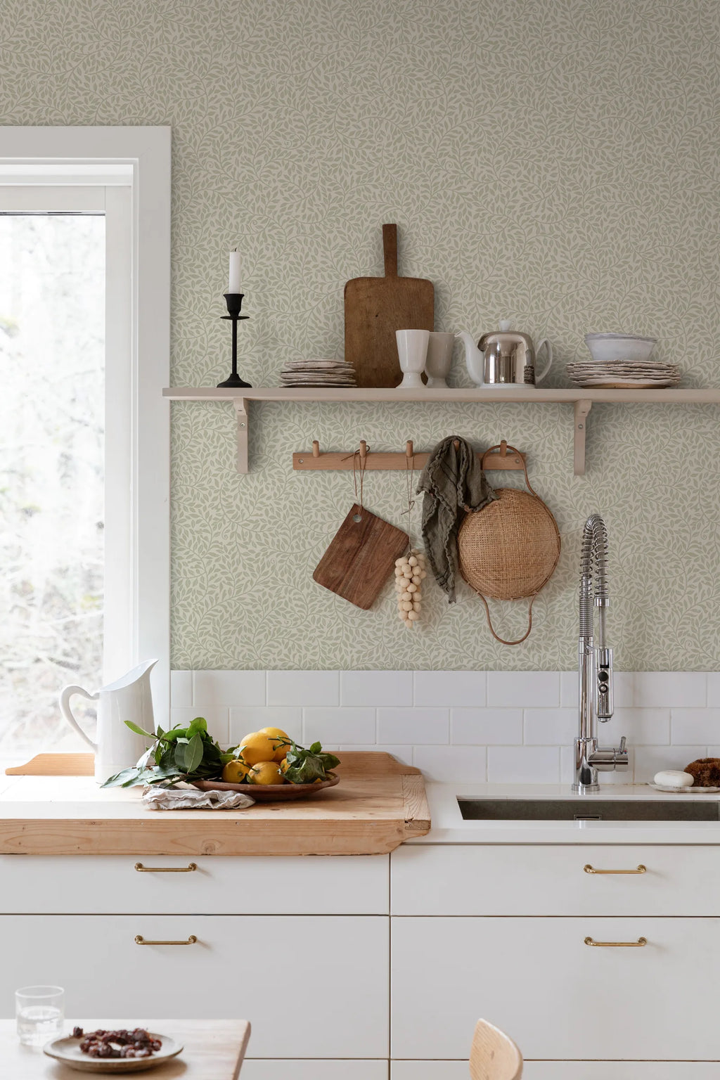 Sigfrid wallpaper by Sandberg in soft green, styled in a bright kitchen above a wooden benchtop with hanging boards and baskets