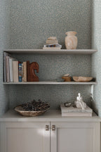 Sigfrid wallpaper by Sandberg in blue-grey, styled behind built-in alcove shelves with books, vases and a brass-knobbed cabinet