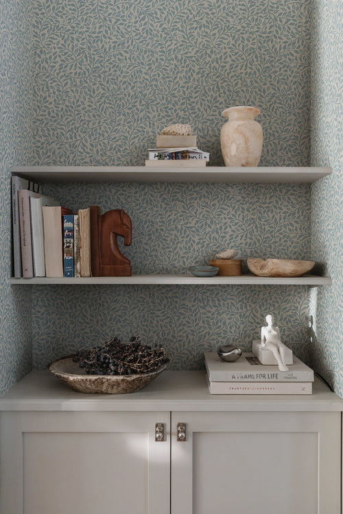 Sigfrid wallpaper by Sandberg in blue-grey, styled behind built-in alcove shelves with books, vases and a brass-knobbed