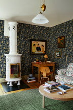 Kvitten wallpaper by Sandberg, navy fruit-and-blossom print in a cosy living room with a white tiled stove and green rug