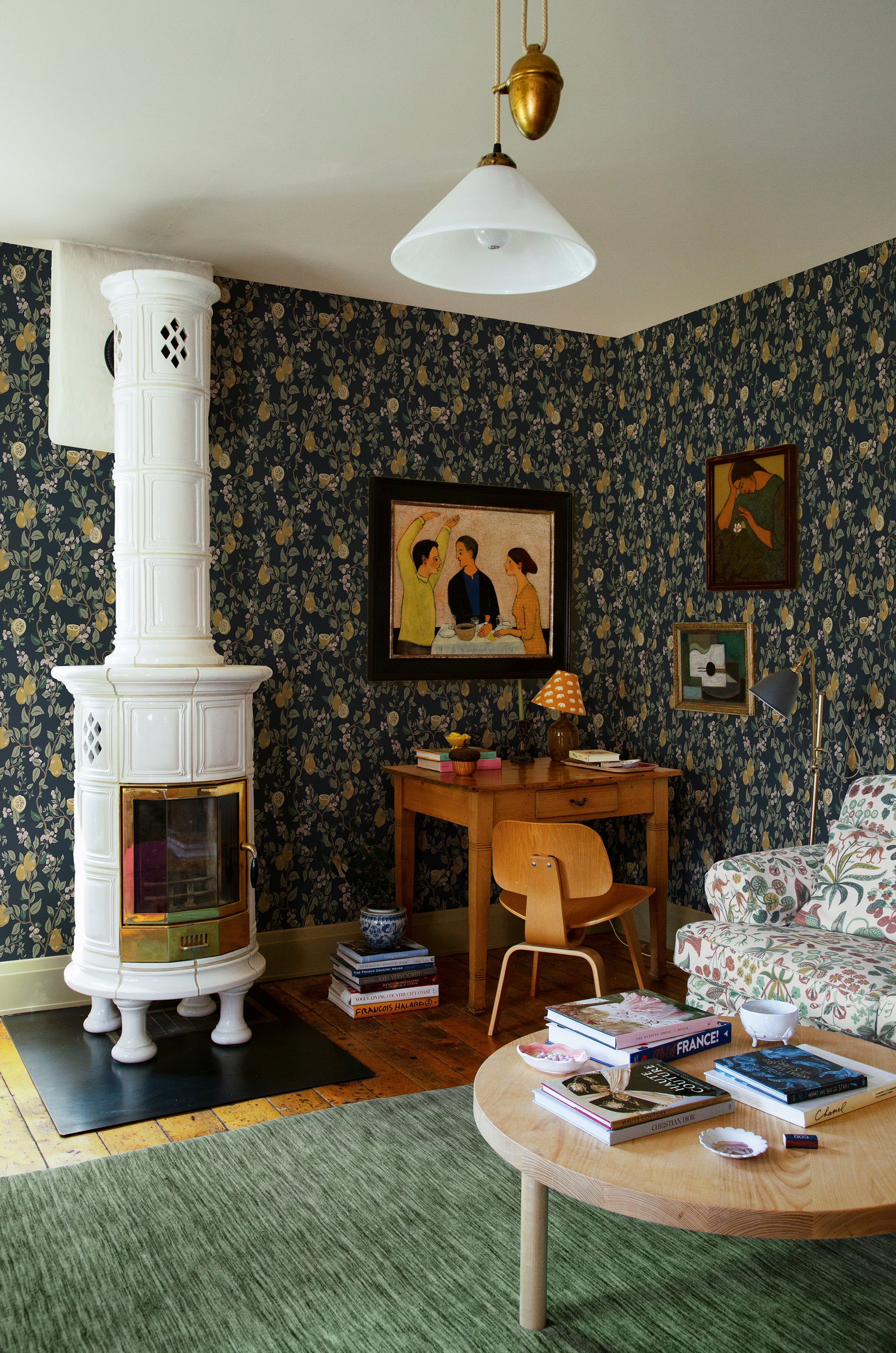 Kvitten wallpaper by Sandberg, navy fruit-and-blossom print in a cosy living room with a white tiled stove and green rug