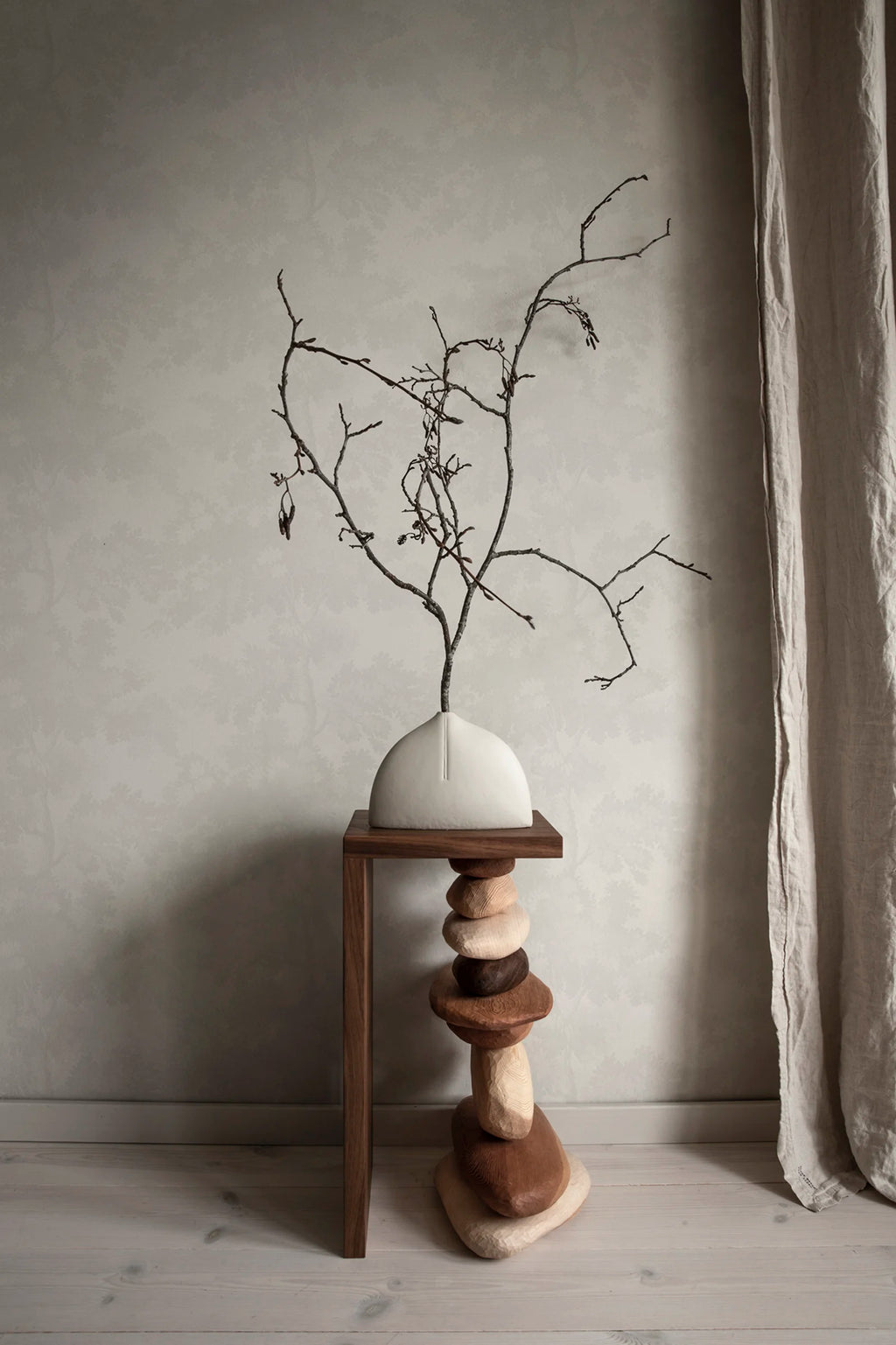Raphael wallpaper by Sandberg in tonal white behind a branch arrangement on a stacked-stone plinth, styled corner