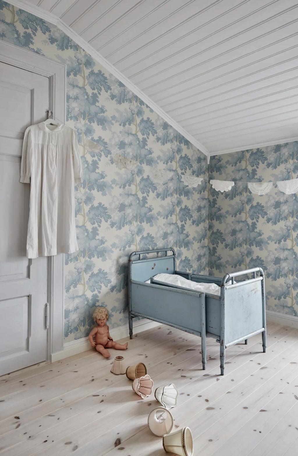 Raphael wallpaper by Sandberg in soft blue oak-tree print in a nursery with a vintage cot and pale floorboards