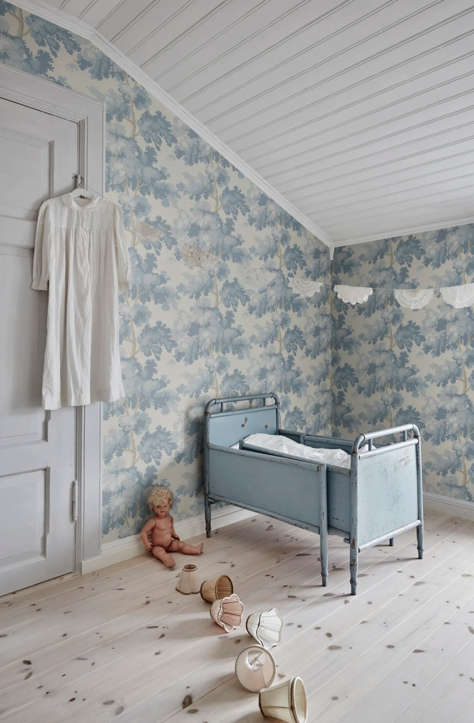 Raphael wallpaper by Sandberg in soft blue oak-tree print in a nursery with a vintage cot and pale floorboards