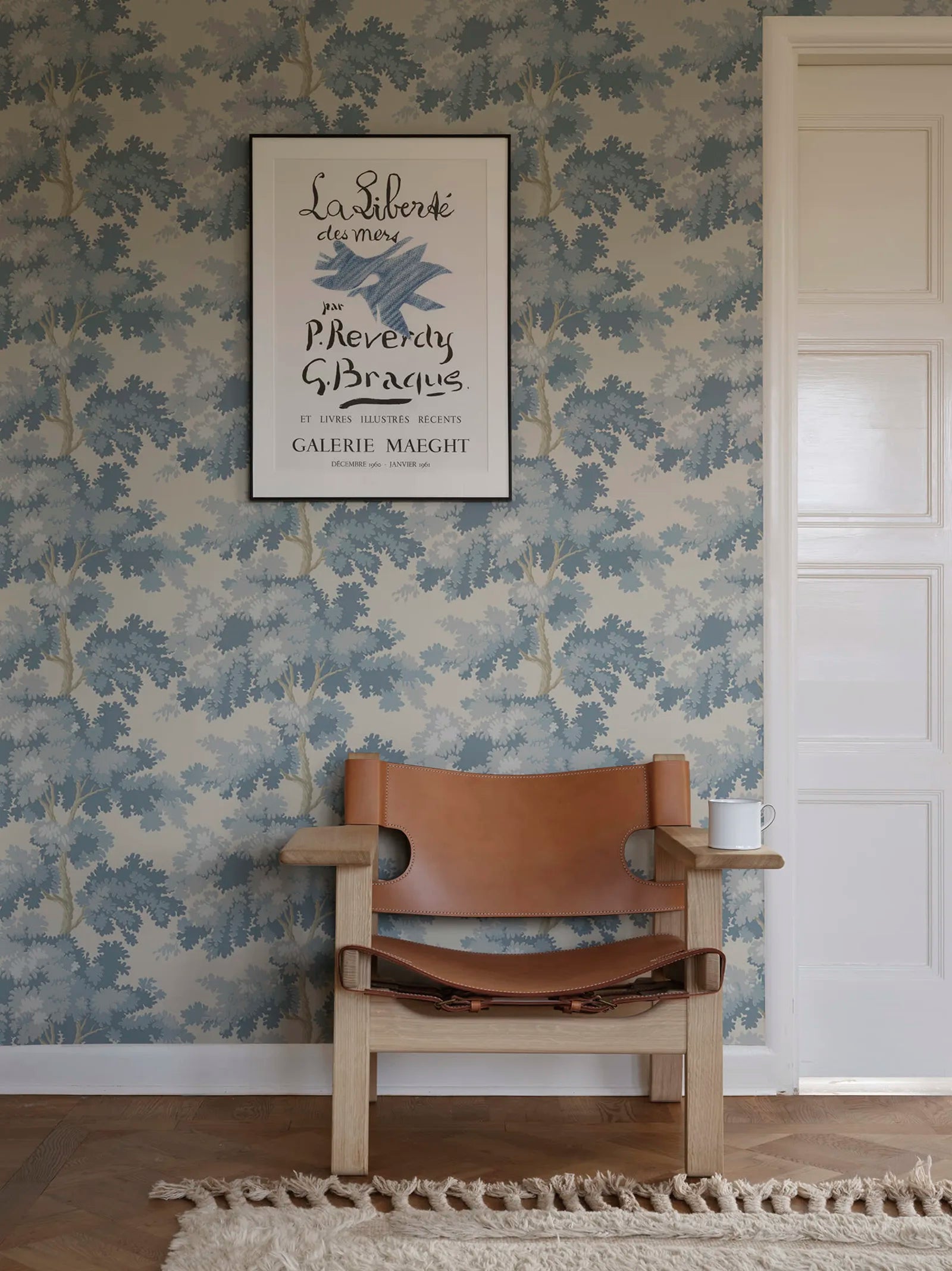 Raphael wallpaper by Sandberg in blue oak-tree print in a hallway with a tan leather chair and framed poster
