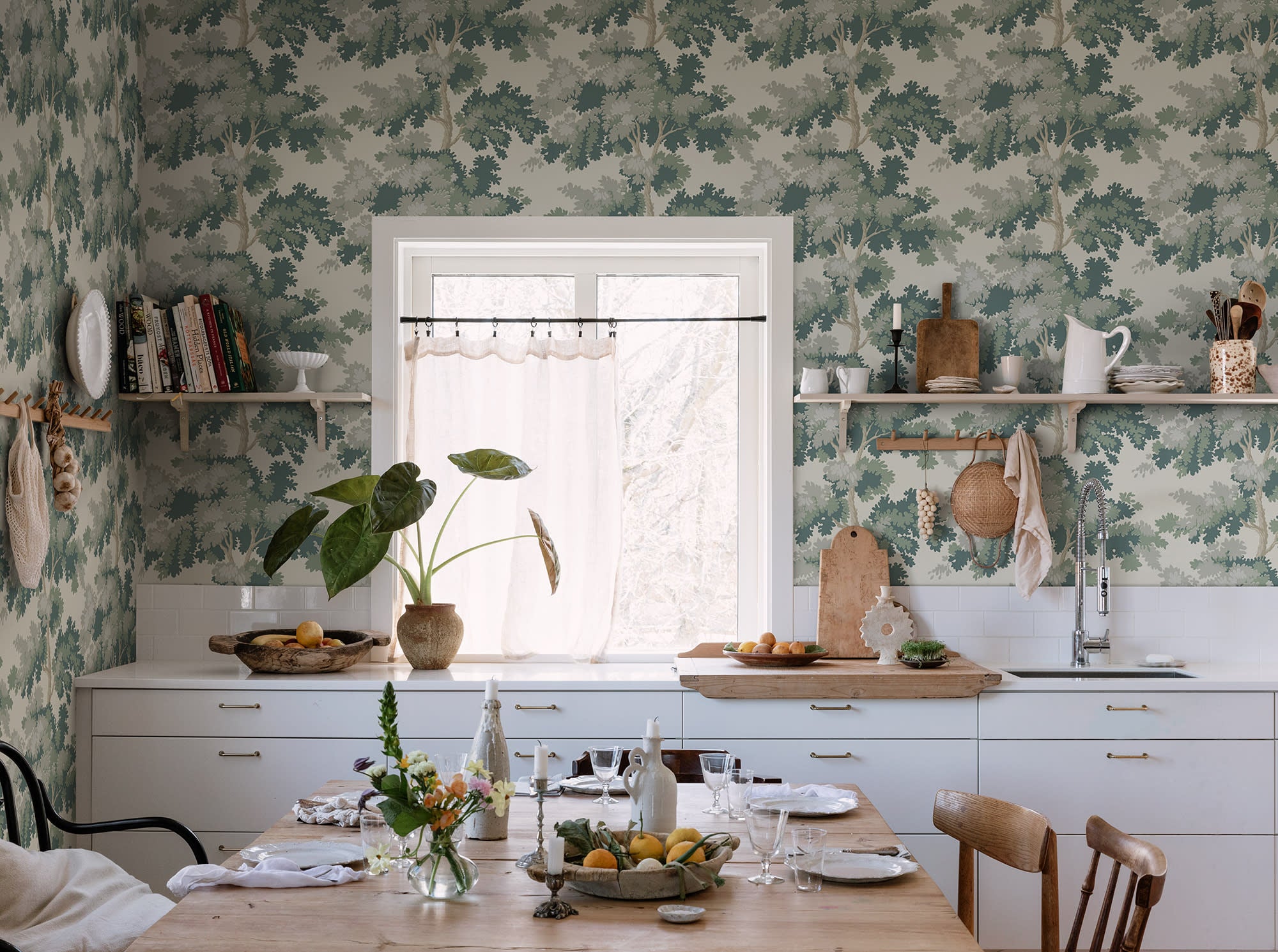 Raphael wallpaper by Sandberg in Green in a kitchen with open shelving, a timber dining table and a cafe curtain