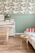 Raphael wallpaper by Sandberg in Green above sage beadboard panelling, with a white piano and wicker chair