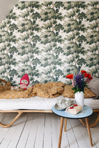 Raphael wallpaper by Sandberg in Green behind a rattan daybed, with a blue side table, cake and cut flowers