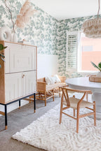 Raphael wallpaper by Sandberg in Green in a dining nook with a round table, wishbone chairs and a rattan pendant