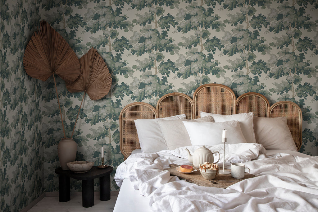 Raphael wallpaper by Sandberg in Green behind a rattan bed head, with white bedding and palm-leaf wall art