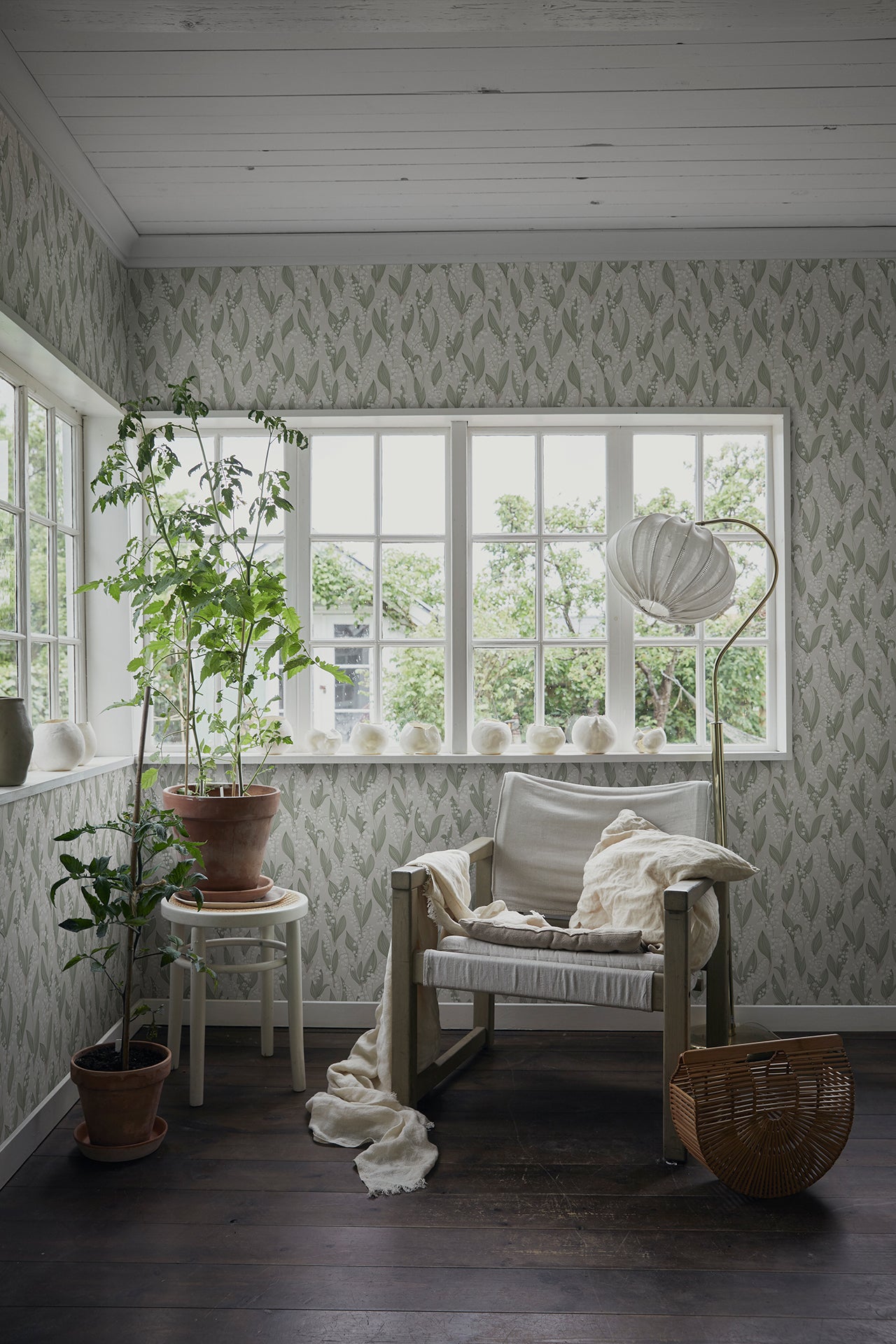 Liljekonvalj wallpaper by Sandberg, lily-of-the-valley print in a bright sunroom with a linen chair and potted plants