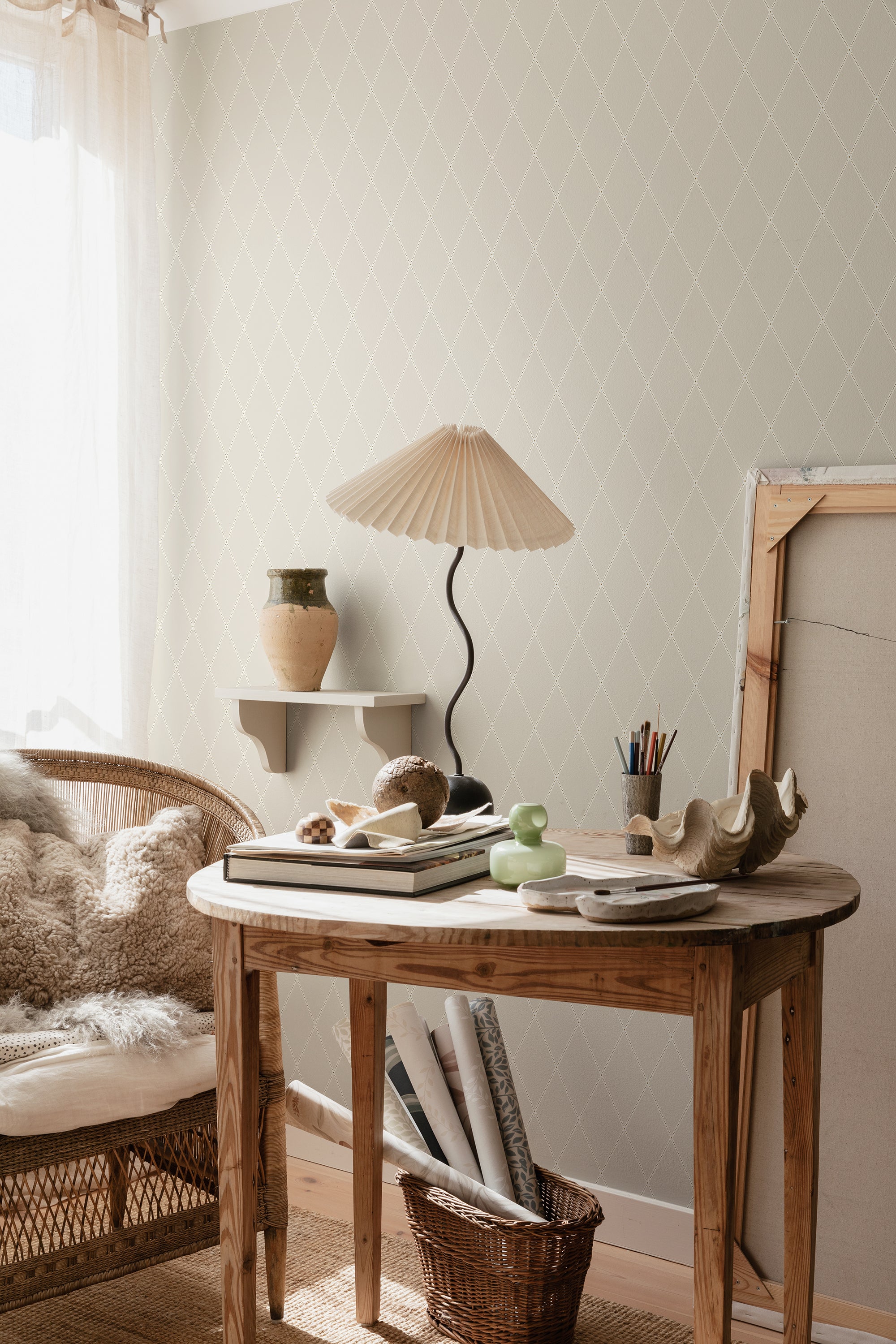 Gabriel wallpaper by Sandberg in pale cream diamond trellis in a sunlit corner with rattan chair and pleated lamp