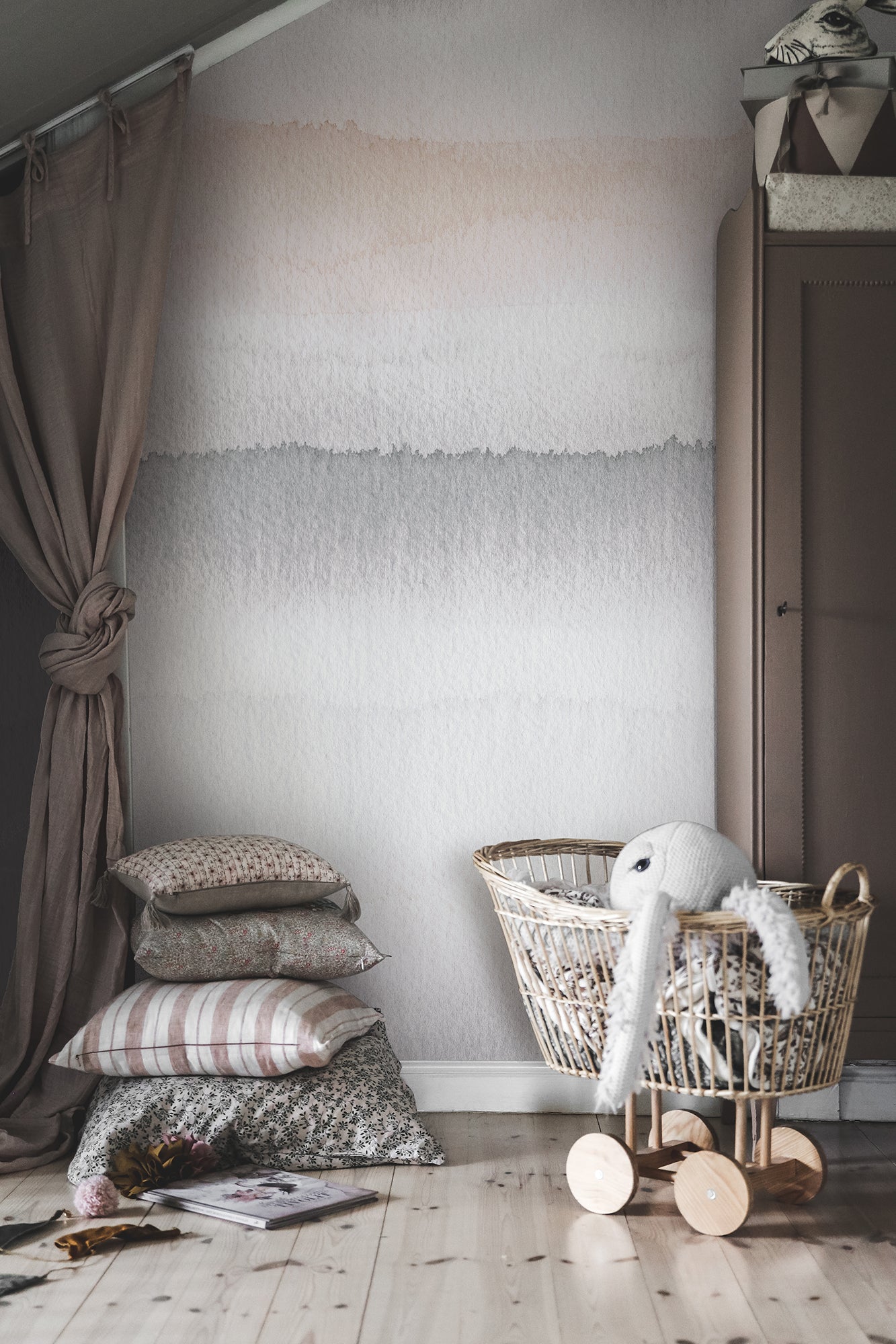 Gryning Dawn wall mural by Sandberg styled in a soft nursery with rattan crib, layered cushions and dusky pink curtain