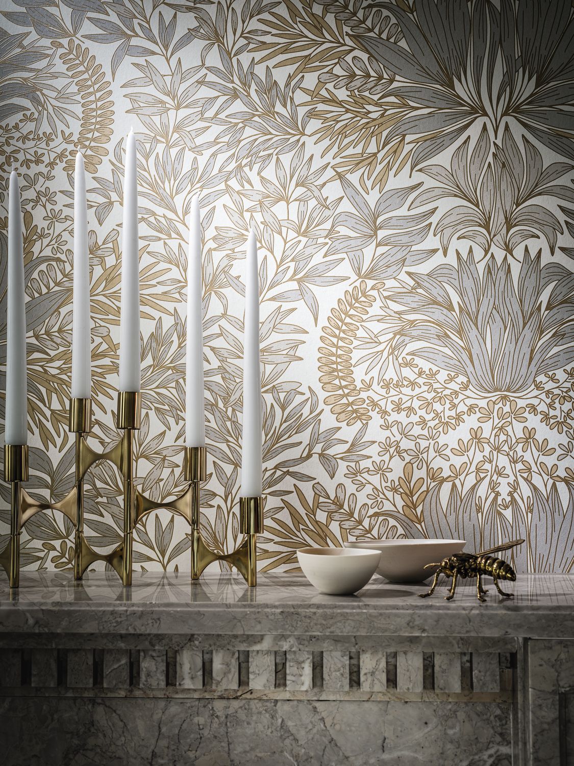 Chardon Floral wallpaper by Casamance in grey and gold, close-up styled above a marble mantel with brass candlesticks