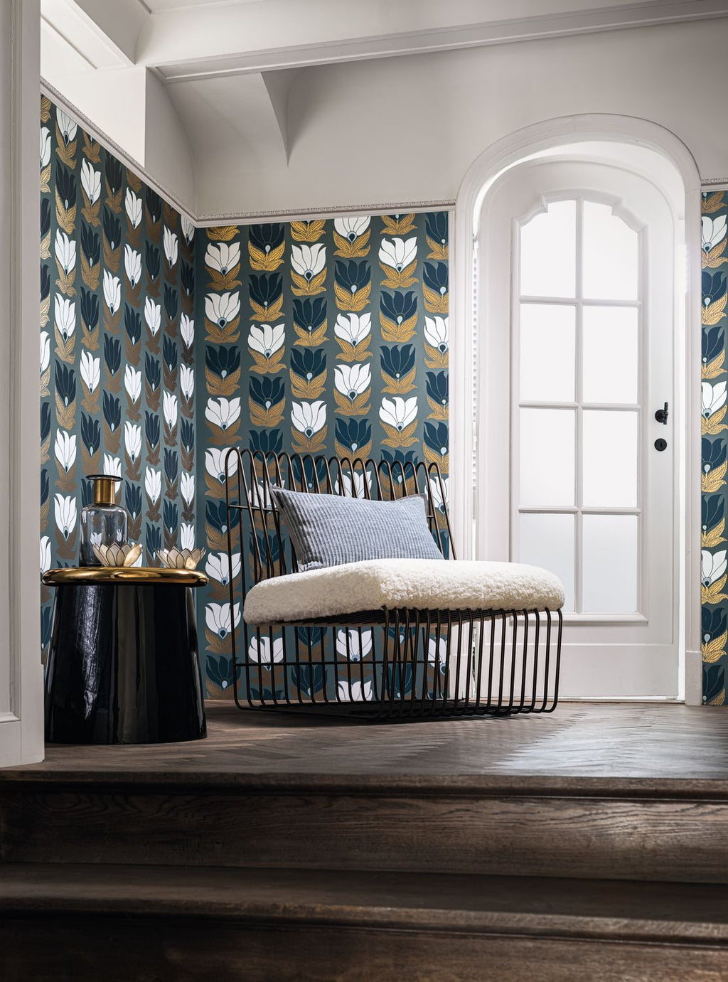 Dauphine wallpaper by Casamance in navy, white and gold on slate blue, styled behind a wire day bed with a sheepskin seat and grey cushion