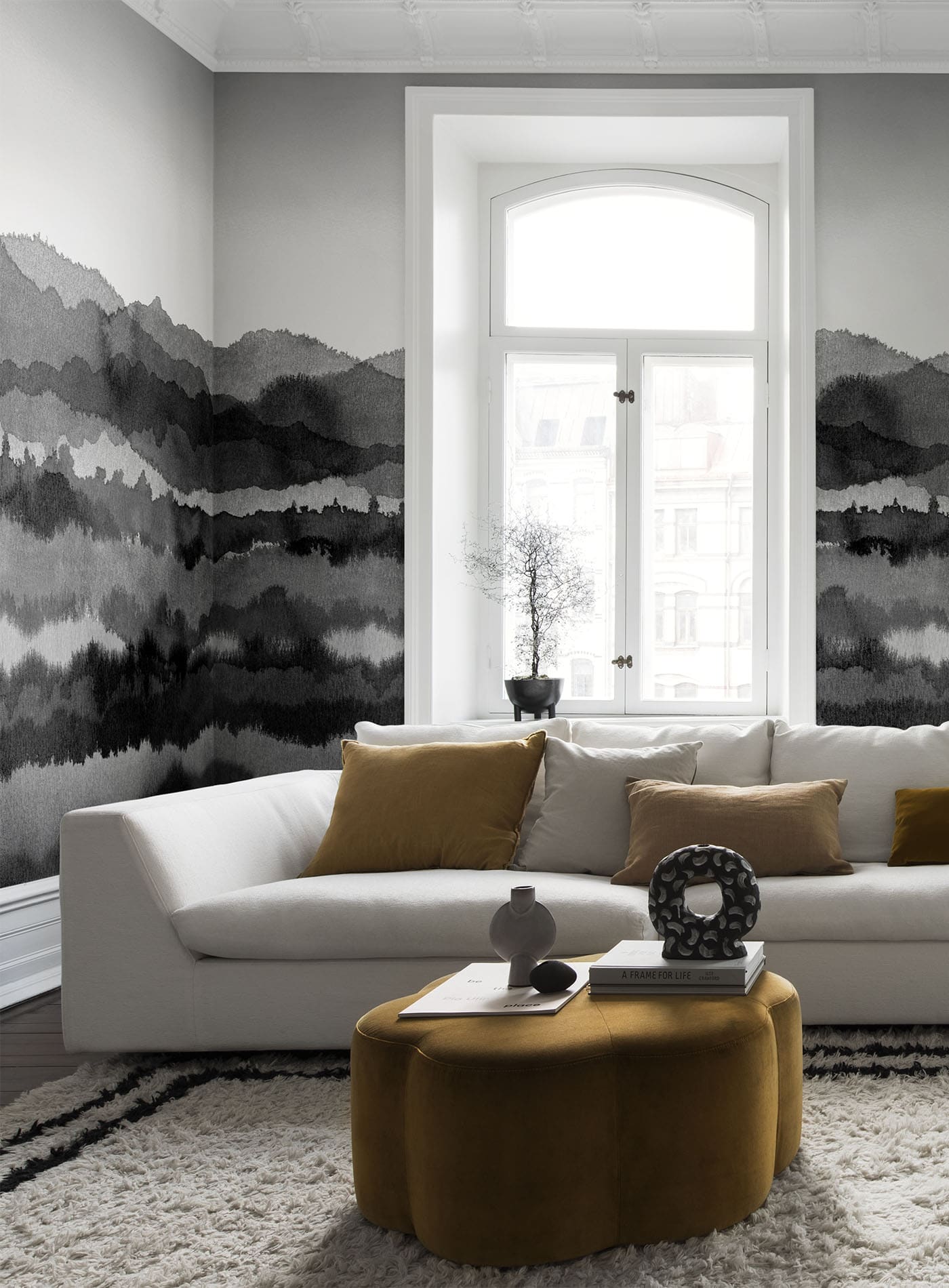 Midnatt wall mural by Sandberg in monochrome grey watercolour layers, wrapping a living room with white sofa and ochre ottoman