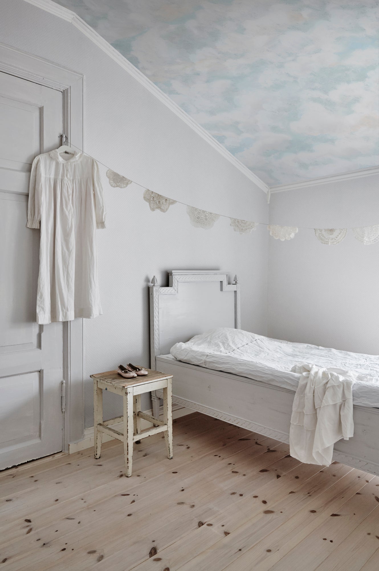 Himmel Clouds wall mural by Sandberg on a sloped bedroom ceiling above a white bed, lace bunting and pine floor