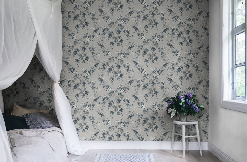 Sandra Floral wallpaper by Sandberg in soft grey, styled in a bedroom behind a white stool holding fresh lilac blooms