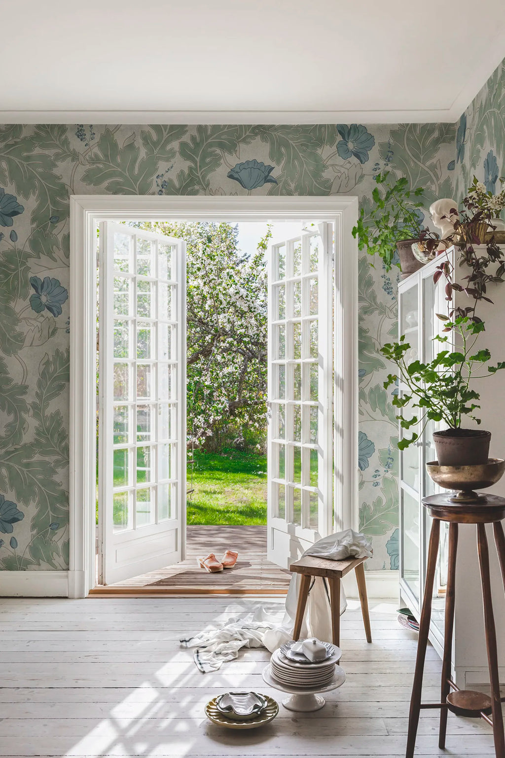 Poppy wallpaper by Sandberg in sage green with blue poppies, styled in a sunlit room with open French doors to a garden